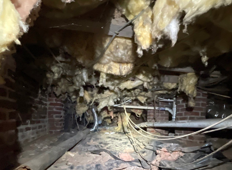 Dark Crawlspace , Old Brick Support, Hanging Insulation and wires, old pipe strewn about the floor